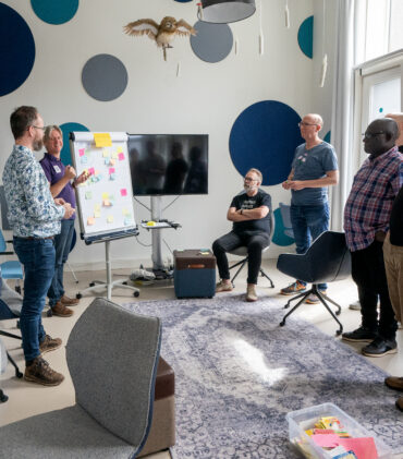 Een groepje medewerkers van TrailBlazers staand rondom een flipover tijdens een TrailBlazers-kwartaalmeeting op 20/8/2024.