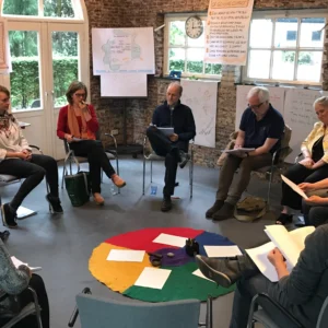 A group of 11 people sitting in a circle, in a workshop setting.