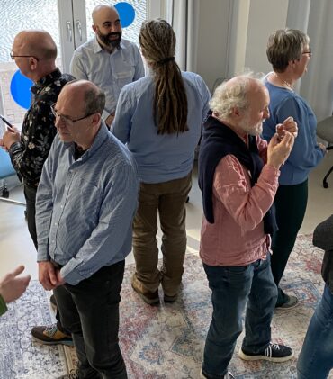 A group of about 10 standing people, that are speaking to each other in pairs.